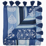 The Malvika Lapis Throw by John Robshaw is a folded blue and white patterned blanket featuring floral and striped designs, hand-printed on 100% cotton voile, adorned with tassels on the edges. - 31272448622638