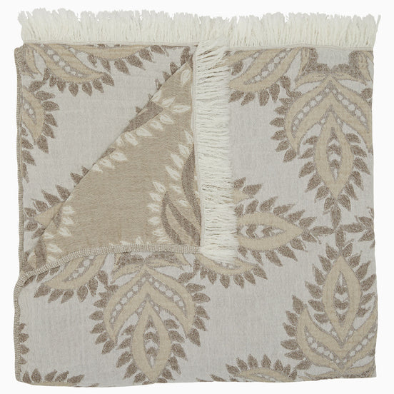 The Dasati Sand Throw by John Robshaw is a beige and white patterned blanket made from stonewashed cotton, featuring fringed edging and partially folded to reveal the woven design on the reverse side.