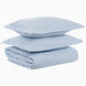 A folded Cinde Light Indigo Organic Duvet and two matching pillows stacked on top of each other against a white background, all crafted from organic cotton duvet material with a 200 thread count percale finish by John Robshaw.
