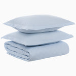 A folded Cinde Light Indigo Organic Duvet and two matching pillows stacked on top of each other against a white background, all crafted from organic cotton duvet material with a 200 thread count percale finish by John Robshaw.