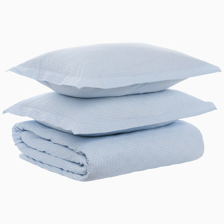 A folded Cinde Light Indigo Organic Duvet and two matching pillows stacked on top of each other against a white background, all crafted from organic cotton duvet material with a 200 thread count percale finish by John Robshaw.