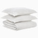 A neatly folded Amina Ecru Duvet Set by John Robshaw and two stacked white pillows with a subtle floral pattern rest on a plain white background, showcasing the finest quality cotton linen.