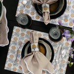 Two table place settings with striped napkins and Nand Metallic Beaded Napkin Rings (Set of 4) from Tabletop, patterned placemats, and grey plates. Glassware and cutlery are neatly arranged, with purple flowers as a decorative touch. - 31307863949358