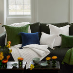 A cozy living room scene with a dark green sofa adorned with various hand quilted pillows and the Velvet White Throw by John Robshaw. Two tables hold vases of flowers and a few small ceramic bowls, evoking the skilled craftsmanship of Indian artisans. - 31307338842158