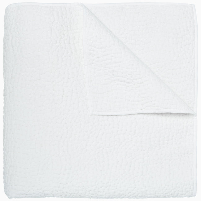 An Organic Hand Stitched White Quilt by John Robshaw folded on top of a white surface.
