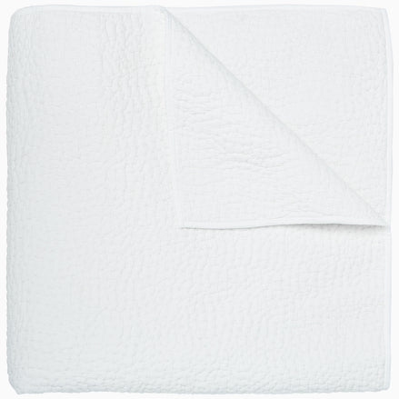 An Organic Hand Stitched White Quilt by John Robshaw folded on top of a white surface.