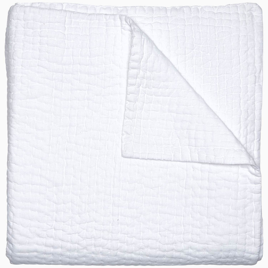 A Vivada White Woven Quilt by John Robshaw folded on top of a white surface with hand stitching.