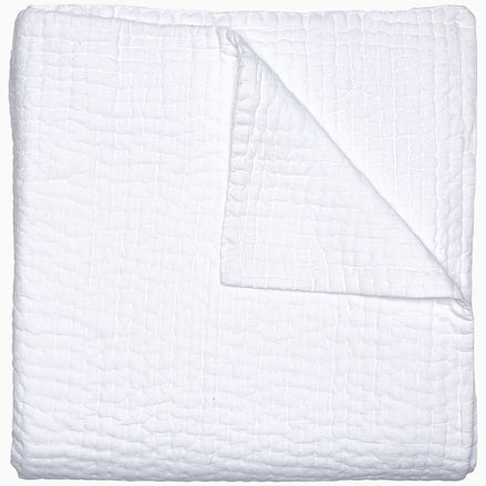 A Vivada White Woven Quilt by John Robshaw folded on top of a white surface with hand stitching.