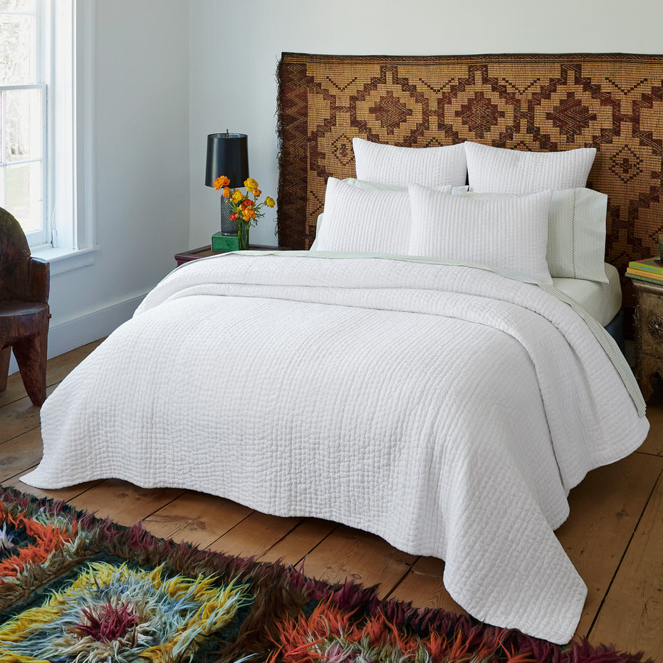 A Vivada White Woven Quilt by John Robshaw in a bedroom with a colorful cotton chambray quilt.