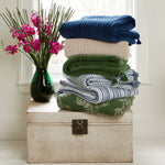 A stack of hand quilted Velvet Moss Throw towels stacked on top of a John Robshaw velvet chest, beautifully crafted by Indian artisans. - 29302498295854