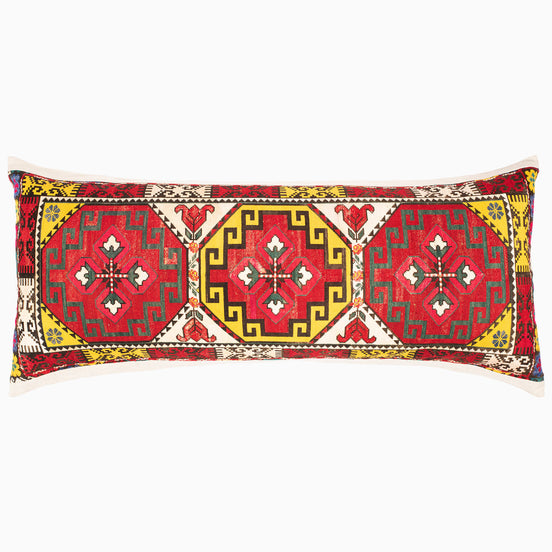 A red and yellow Sai Bolster pillow with a geometric design inspired by tribal motifs from the Swat Valley, created by John Robshaw.