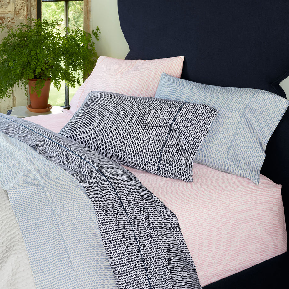 A 100% cotton percale bed with blue, pink, and white bedding, including a John Robshaw Cinde Light Indigo Organic Sheet Set.