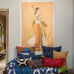 A living room with a vintage sofa, hand-painted pillows, and a John Robshaw Princess With Instrument Tapestry wall hanging. - 30148787765294