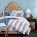 A Custom Dara Bed with blue and white bedding and a John Robshaw wicker basket available for white glove delivery.
