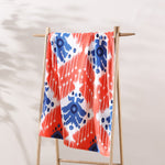 A John Robshaw Sashpura Coral Beach Towel hanging on a wooden rack. - 29274373947438