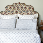 A bed with an ornate headboard and pillows made of a Kama Gray Organic Sheet Set from John Robshaw. - 30264085250094