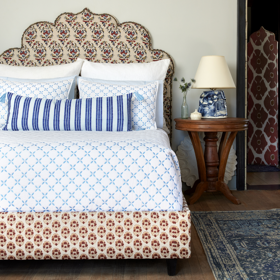 A Layla Azure Quilt bed with a blue and white patterned headboard inspired by Mughal gardens, designed by John Robshaw.