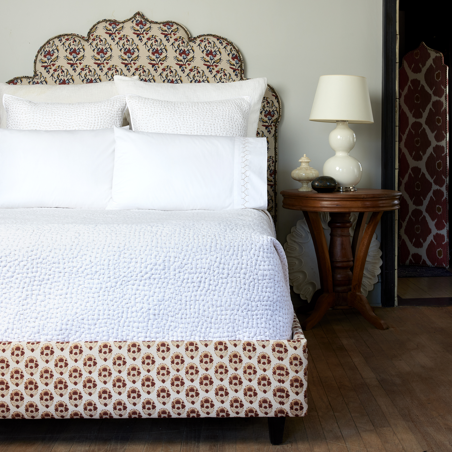 A white bed with an ornate headboard made of John Robshaw's Organic Hand Stitched Sand Quilt.