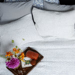 An indigo bed with pillows and a tray with flowers on it, adorned with a Cinde Indigo Organic Sheet Set by John Robshaw. - 28362850205742