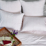 A bed with Poseti Lotus Organic Sheet Set made by John Robshaw, adorned with fluffy pillows and a book waiting to be read. - 28311596662830