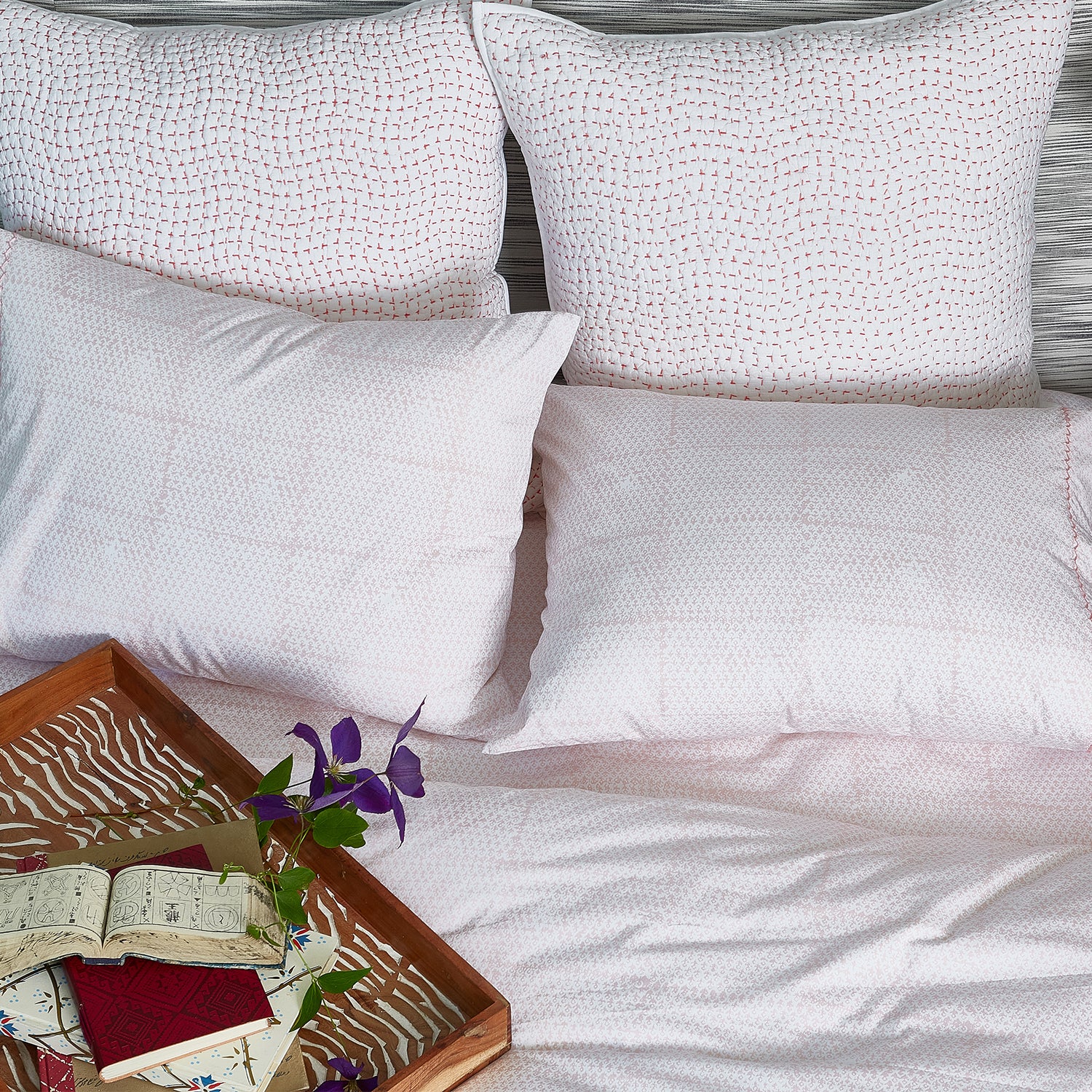 A bed with Poseti Lotus Organic Sheet Set made by John Robshaw, adorned with fluffy pillows and a book waiting to be read.