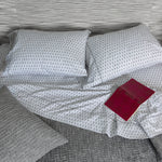 A John Robshaw Kama Gray Organic Sheet Set bed with pillows and a book on it. - 28311597744174