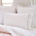 A bed with Stitched Ink Organic Sheets by John Robshaw and a white comforter with embroidered designs. - 30273372651566