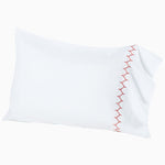 A white pillow with red embroidery stitching on Stitched Coral Organic Sheets by John Robshaw. - 30273362624558
