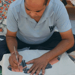 A man is hand painting an elephant on a piece of paper, inspired by the Two Elephants Decorative Pillow design by John Robshaw. - 28009963716654