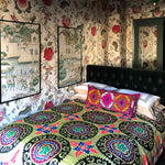 A Tashkent Guide bed in a room with floral wallpaper adorned with Uzbekistan suzanis, an intricately embroidered tribal textile. (Brand Name: John Robshaw) - 15404298174510